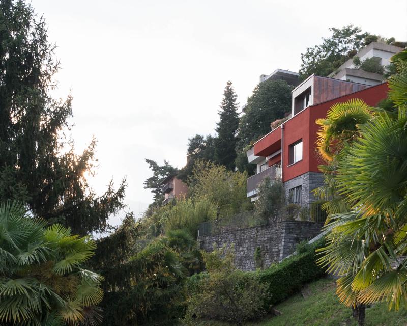 Conversion of holiday home Casa Sogno Mio, Locarno Painted in KEIM oxide red and with new dormer on a stone base, surrounded by palms 