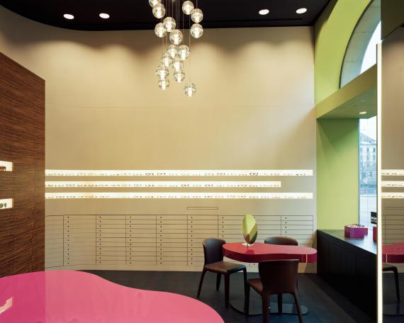 Müller Optik optician store showroom with consulting tables in pink and eyewear display wall at the back