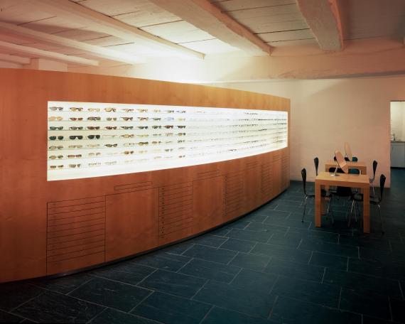 Dudli Optik optician store showroom with curved eyewear display wall and consulting tables