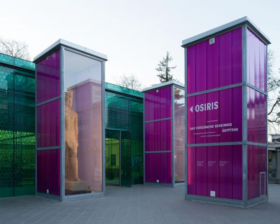 Osiris exhibition Museum Rietberg Three enclosures in hot-dip galvanised steel and polycarbonate panels in violet with the colossal statue of the king in front of the emerald building