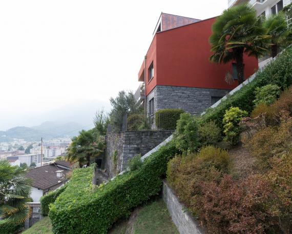 Conversion of holiday home Casa Sogno Mio, Locarno Painted in KEIM oxide red and with new dormer on a stone base, surrounded by palms 