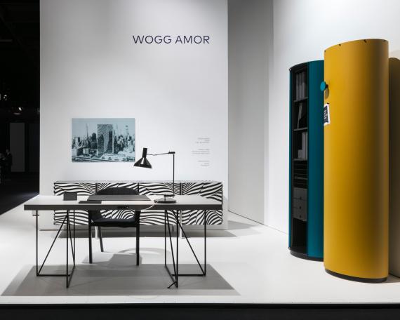 Möbelmesse Köln 2017 Wogg Amor Kollektion Litfass-Säule Stripe Sideboard Moderato Arbeitstisch Sessel vor weisser Wand mit Bild von Trix und Robert Haussmann