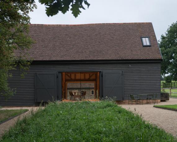 Conversion of barn at Chapel House Farm, Oakwood Hill, Surrey View across the flowerbed to the barn with open doors and Sky-Frame sliding windows