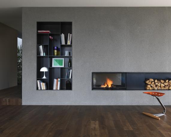 Sandblasted concrete core with black-steel shelving and tunnel fireplace by Cheminée Stutz, with a black-steel surround 