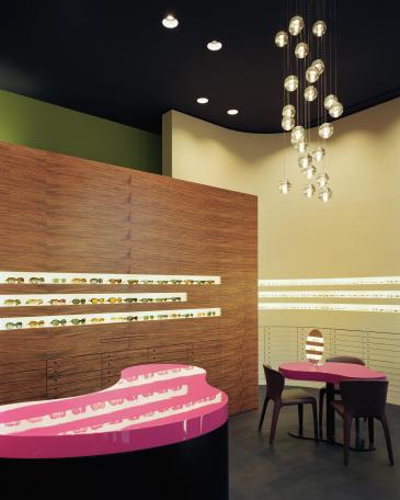 Müller Optik optician store showroom eyewear display wall in ovangkol and coloured consulting tables