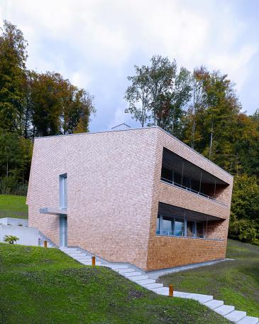 House Tuggen on the edge of the forest with wooden shingles in red cedar and loggia