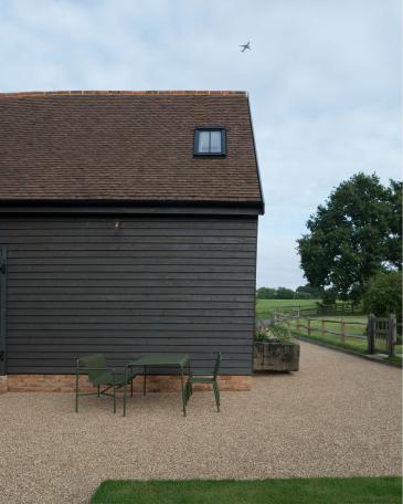 Umbau Scheune Chapel house farm in Oakwoodhill Surrey Detail Hay Palissade Gartenmöbel vor  vorvergraute Holzstülpschalung über einem Sichtbacksteinmauerwerk und Ziegeldach 