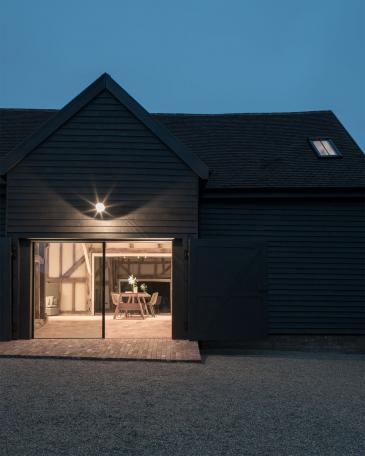 Umbau Scheune Chapel house farm in Oakwoodhill Surrey Abendstimmung und Blick durch die Sky-Frame Fenster in den Innenraum mit Fachwerk und hexagonalen Terrakottaplatten 