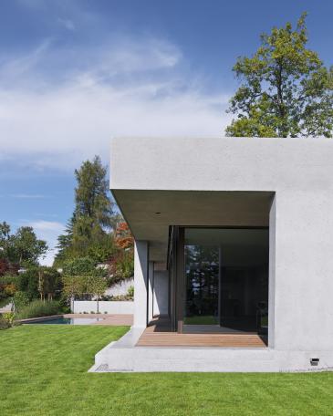 South façade with covered seating area, recessed terrace and view towards the pool and surrounding decking by Woodtli Schwimmbadtechnik 