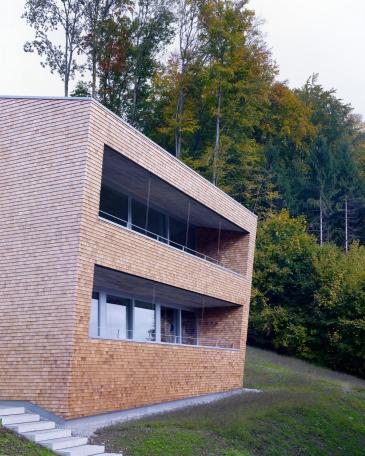 House Tuggen on the edge of the forest with wooden shingles in red cedar and loggia