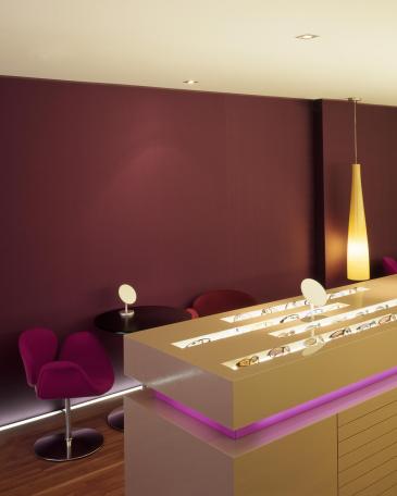 Urech Optik optician store backlighted display furniture in front of a wallcovering in fabric at the consulting area
